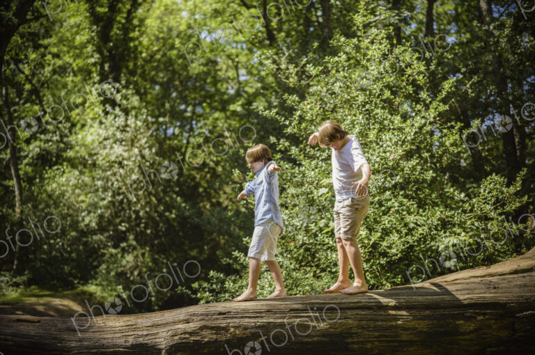 Two boys camping in the New Forest. Walking along a log above the water, balancing…