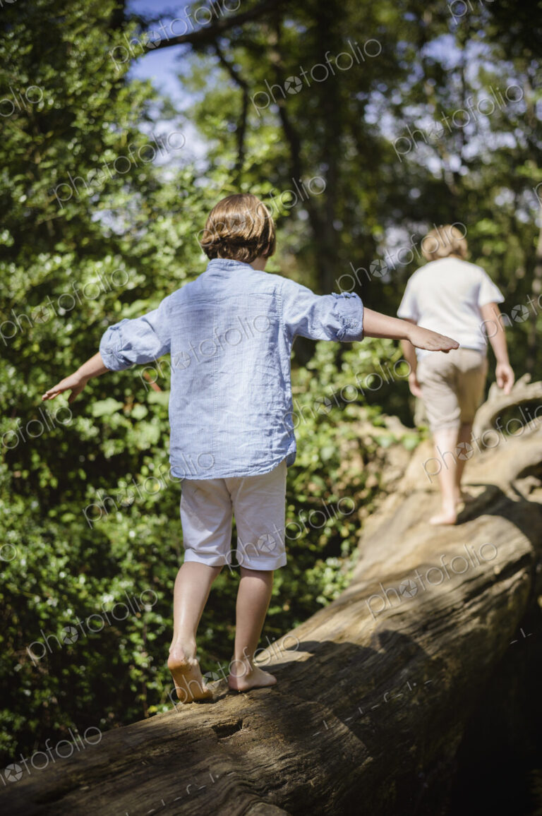 Two boys camping in the New Forest. Walking along a log above the water, balancing…
