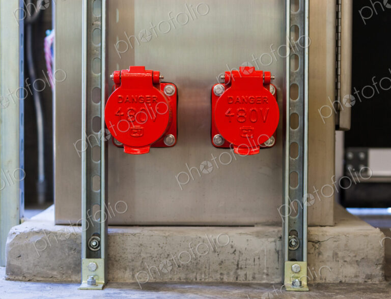 Two bright red plastic covers, caps covering electricity power points on a wall, sign…