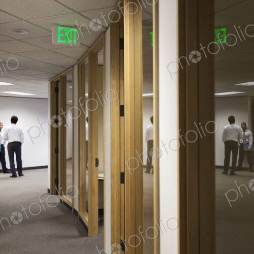 Two business men standing and talking at the end of an office hallway. Two business men standing and talking at the end of an office hallway.
