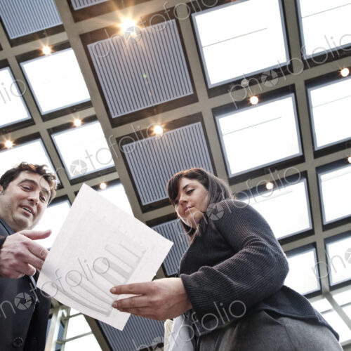 Two business people going over paperwork in a large convention center lobby.