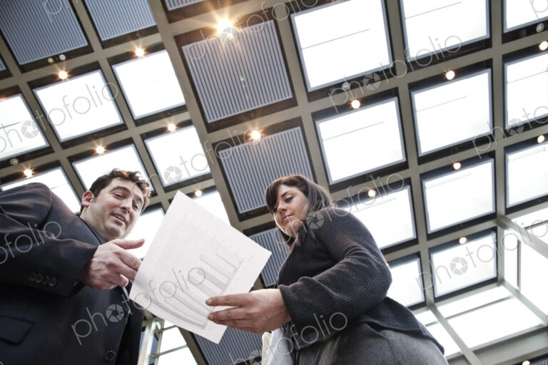Two business people going over paperwork in a large convention center lobby.