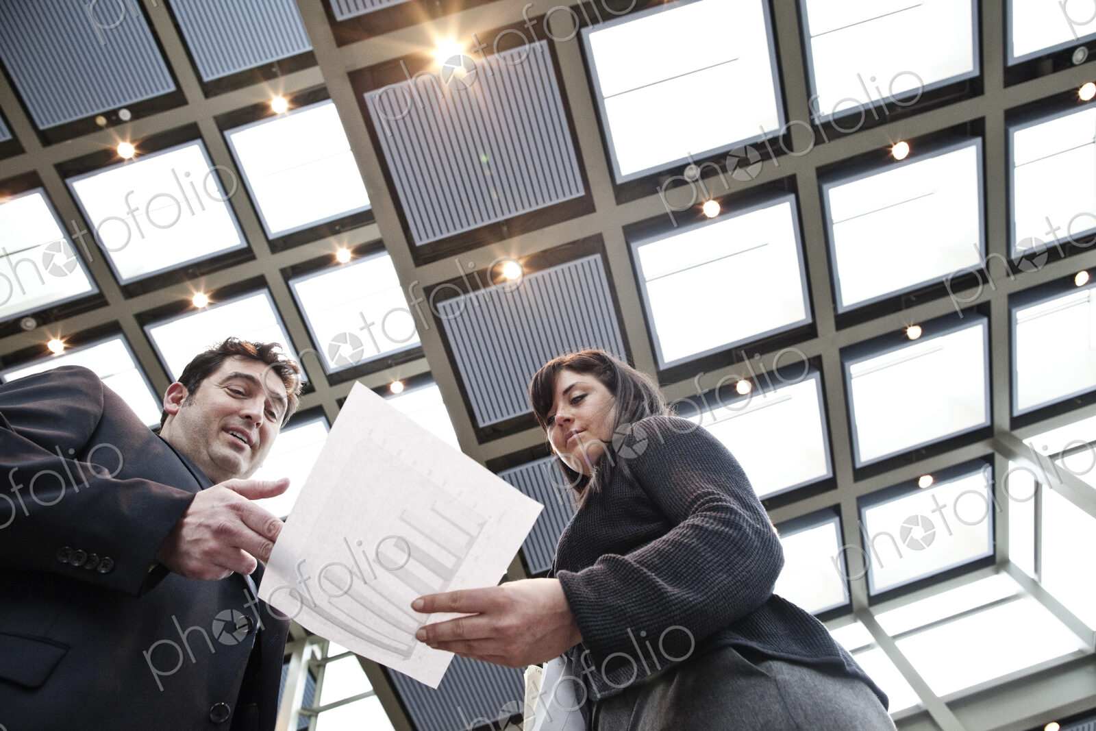 Two business people going over paperwork in a large convention center lobby.