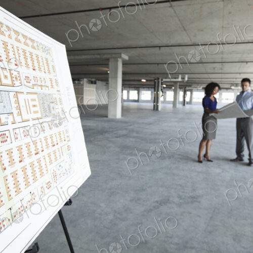 Two business people in a new raw office space with an office floor plan in the foreground.