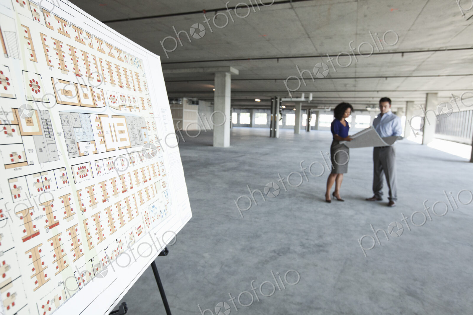 Two business people in a new raw office space with an office floor plan in the foreground.