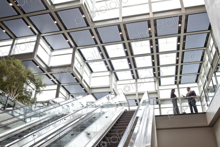 Two business people meeting at the top of an escalator in a large convention center lobby