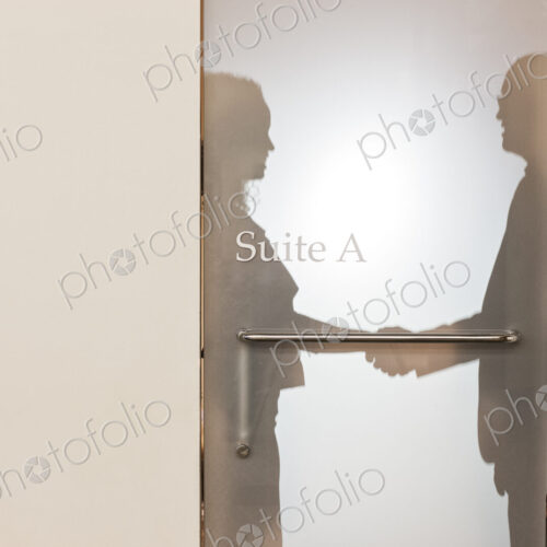 Two business people shaking hands and silhouetted through the frosted glass door of an… Two business people shaking hands and silhouetted through the frosted glass door of an…