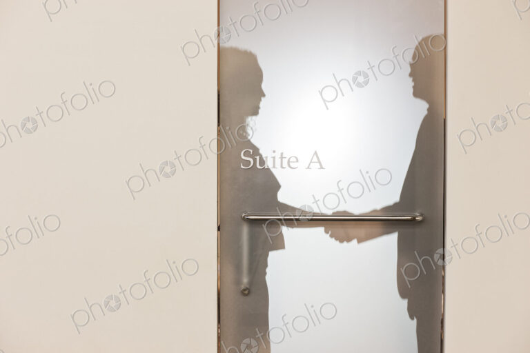 Two business people shaking hands and silhouetted through the frosted glass door of an…
