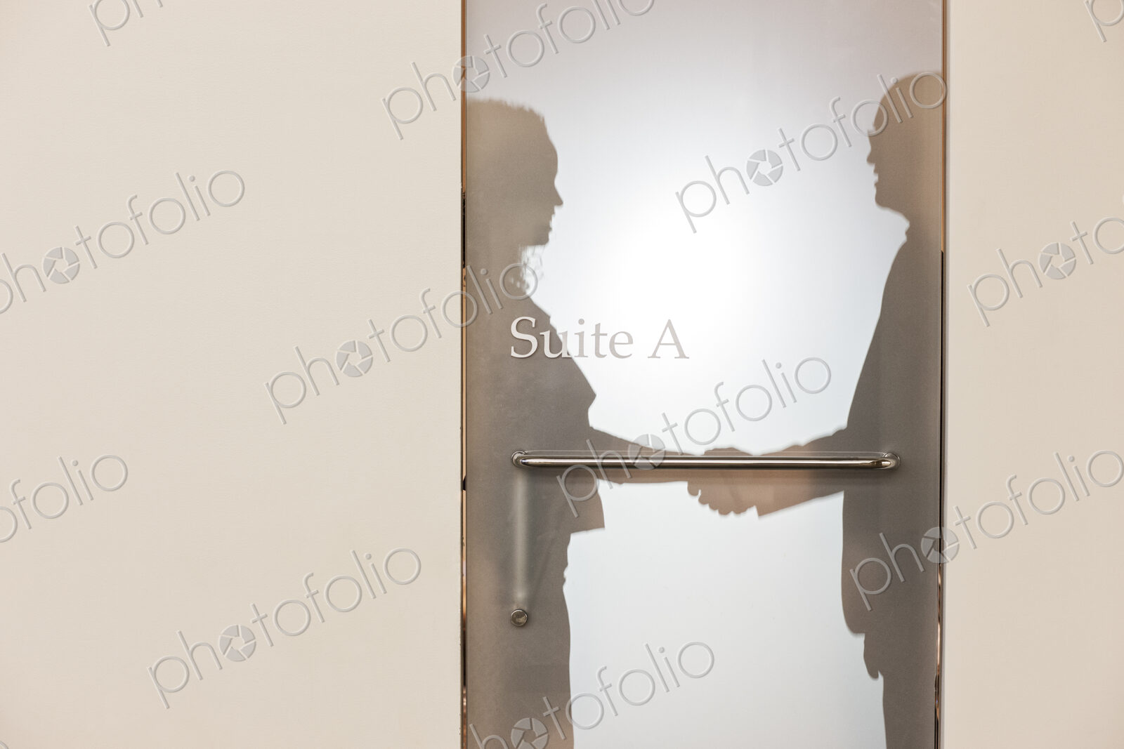 Two business people shaking hands and silhouetted through the frosted glass door of an…