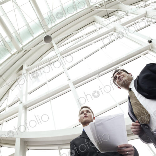 Two businessmen going over paperwork in the lobby of a large convention center.