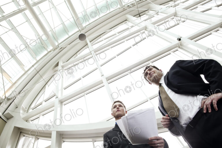 Two businessmen going over paperwork in the lobby of a large convention center.