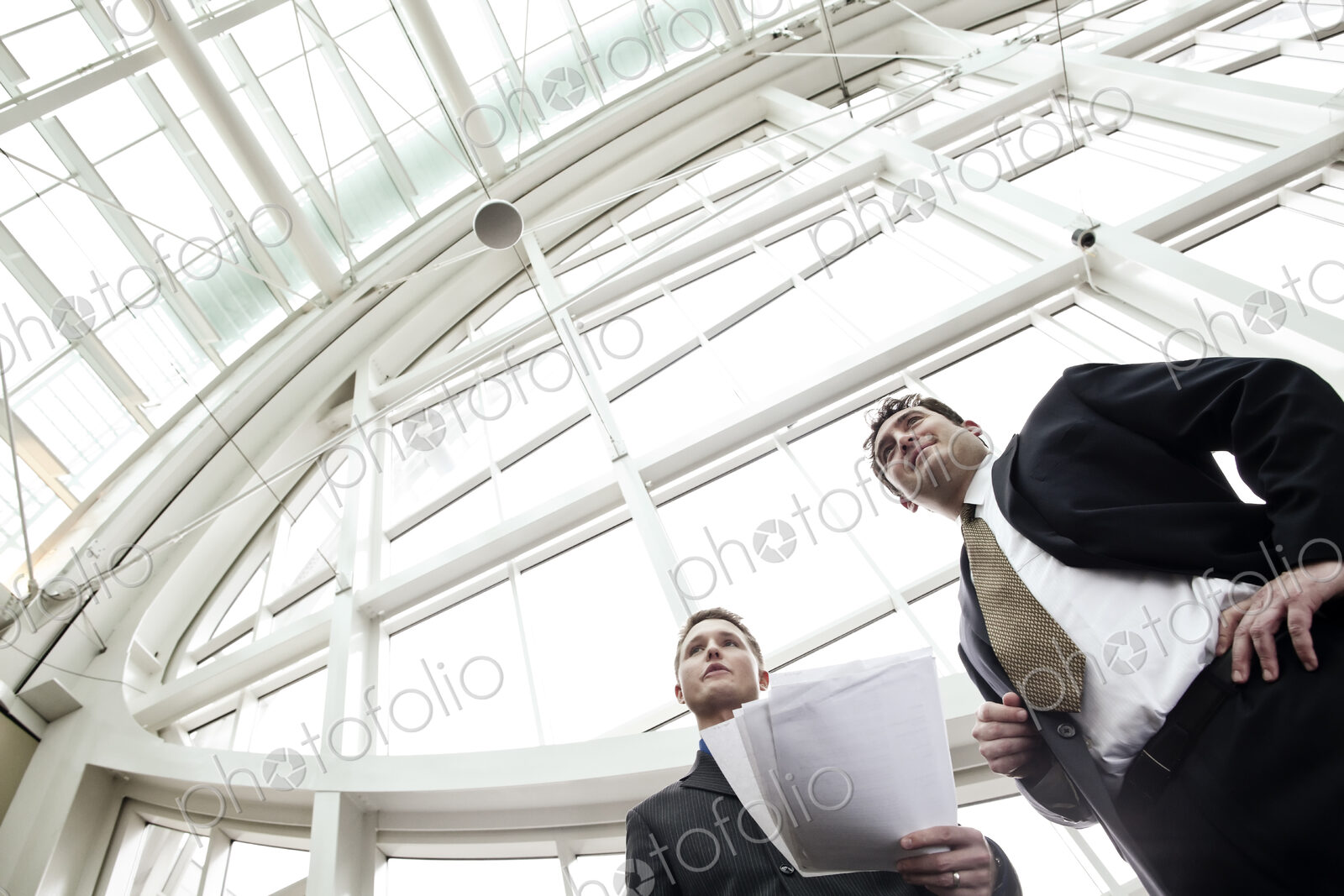 Two businessmen going over paperwork in the lobby of a large convention center.