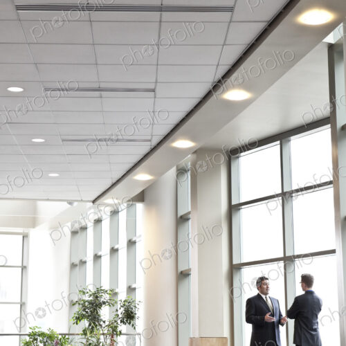 Two businessmen meeting in front of a window in a large convention center lobby. Two businessmen meeting in front of a window in a large convention center lobby.