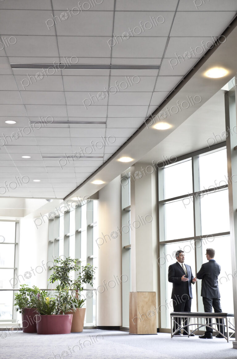 Two businessmen meeting in front of a window in a large convention center lobby.