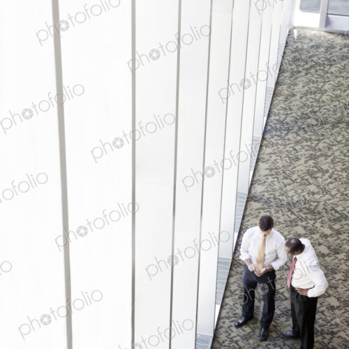 Two businessmen meeting next to a large bank of windows in a business center. Two businessmen meeting next to a large bank of windows in a business center.