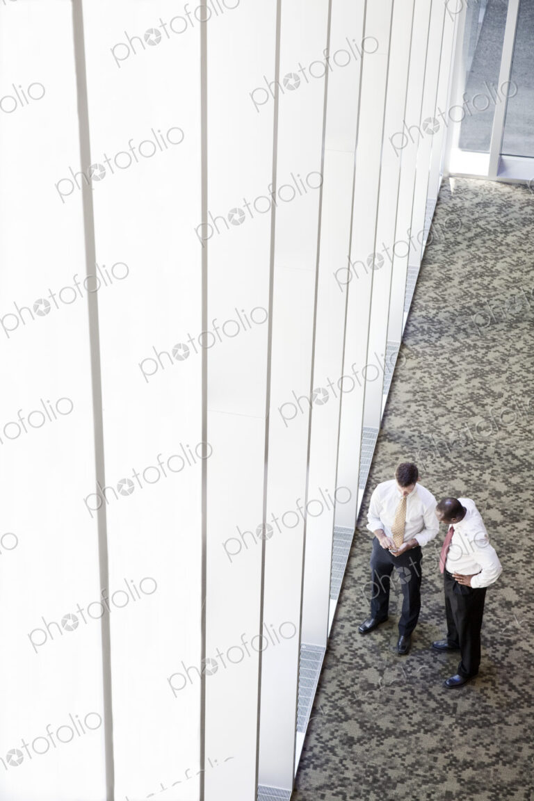 Two businessmen meeting next to a large bank of windows in a business center.