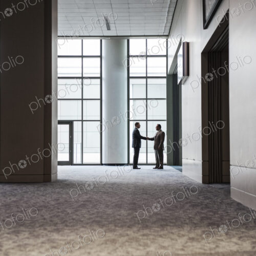 Two businessmen silhouetted and shaking hands in front of a large convention center… Two businessmen silhouetted and shaking hands in front of a large convention center…