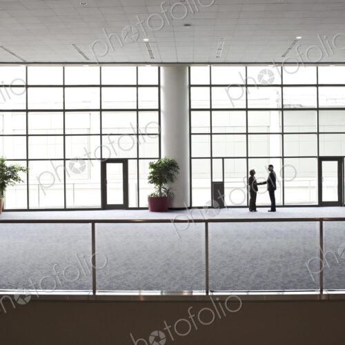 Two businessmen silhouetted and shaking hands in front of a large convention center…