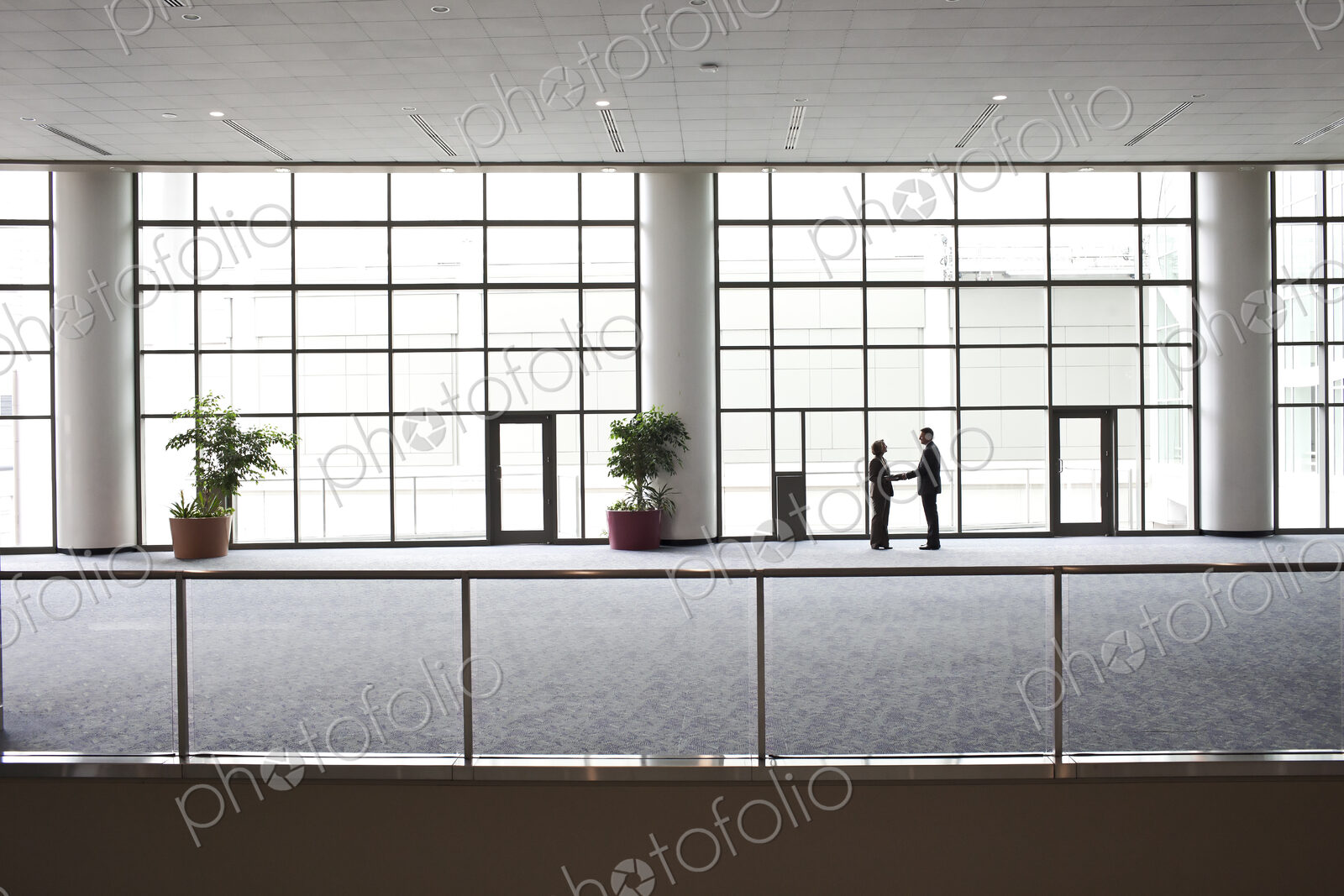 Two businessmen silhouetted and shaking hands in front of a large convention center…