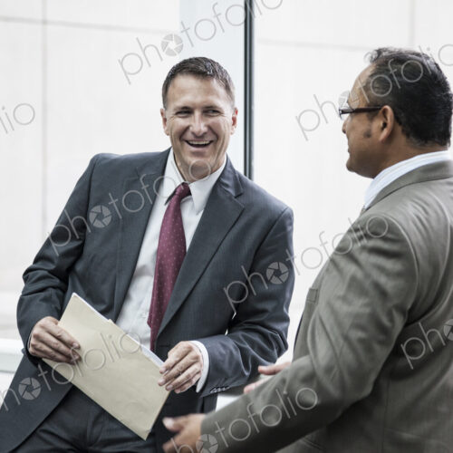 Two businessmen standing chatting in an open area of an office building.