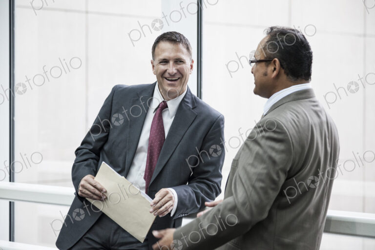Two businessmen standing chatting in an open area of an office building.