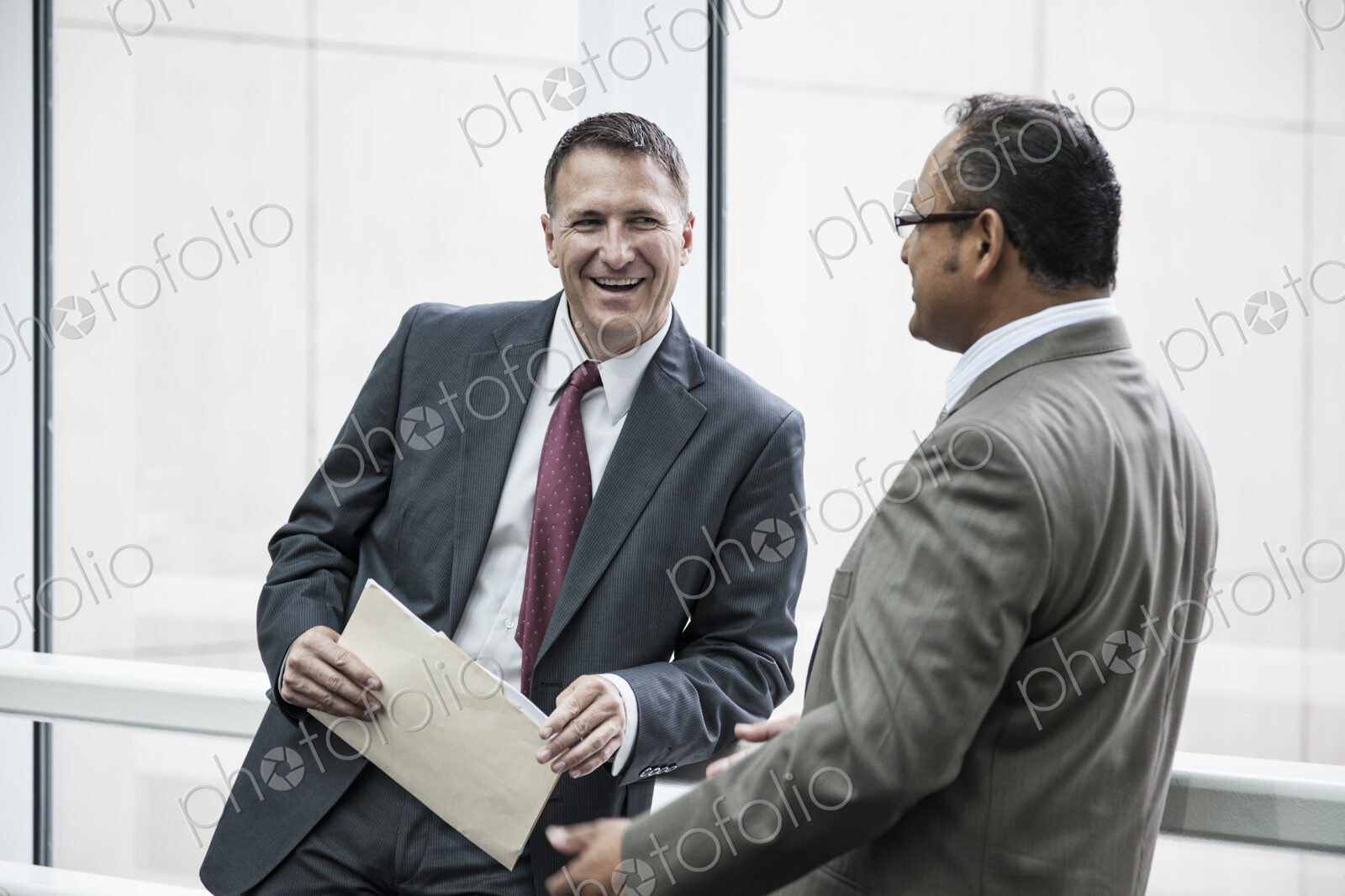 Two businessmen standing chatting in an open area of an office building.