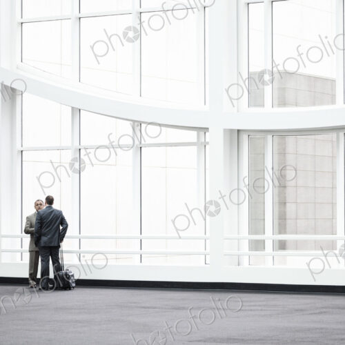 Two businessmen standing in a glassed in lobby area of a convention center. Two businessmen standing in a glassed in lobby area of a convention center.