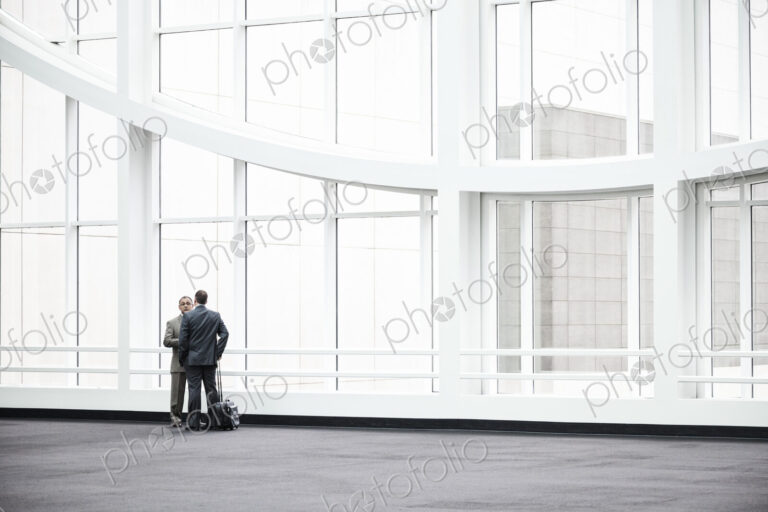 Two businessmen standing in a glassed in lobby area of a convention center.