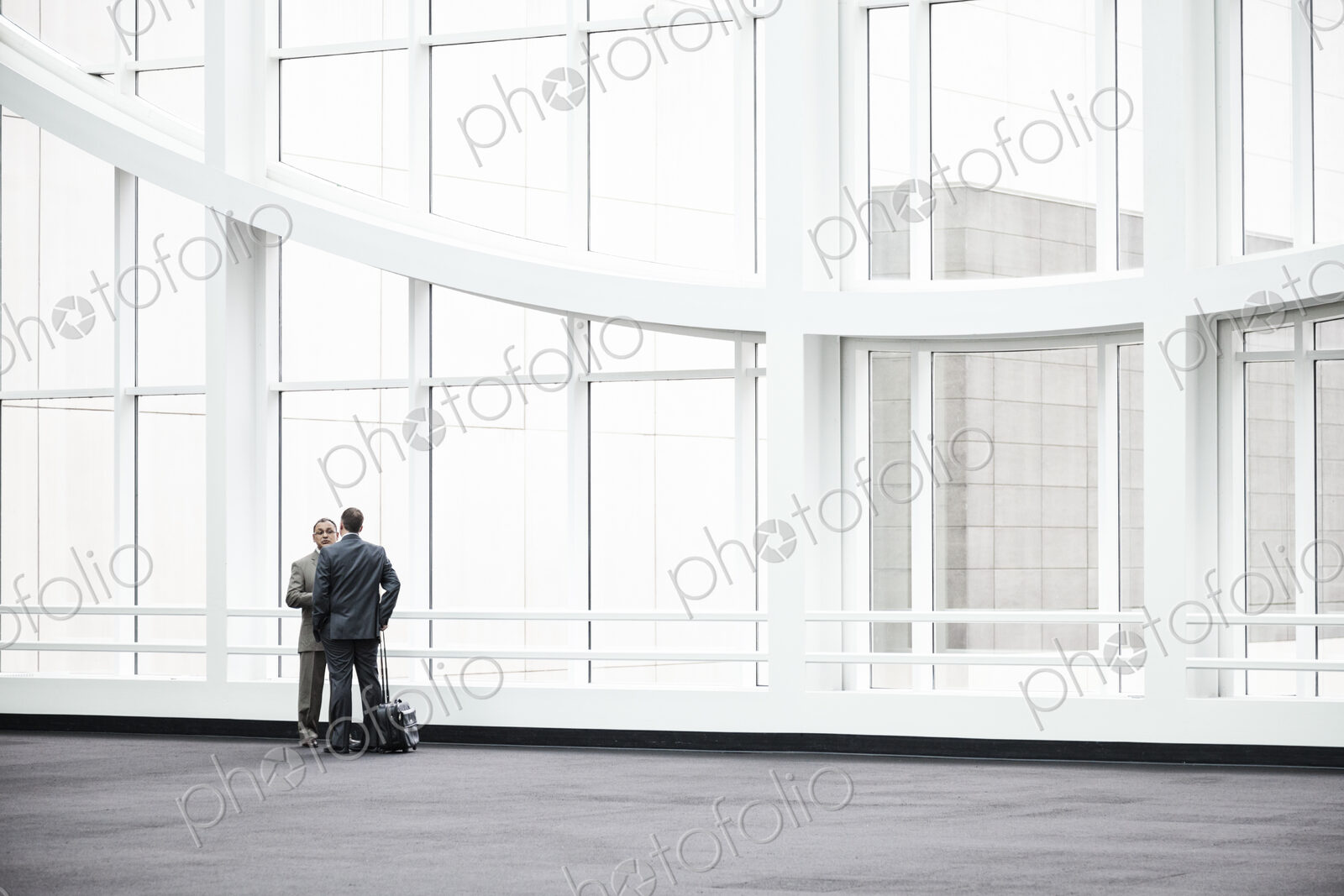 Two businessmen standing in a glassed in lobby area of a convention center.