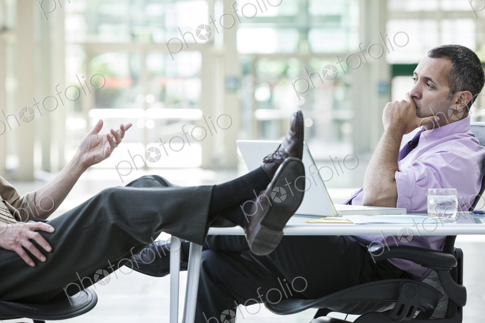 Two businessmen talking at a desk with one person’s feet resting on top of the table