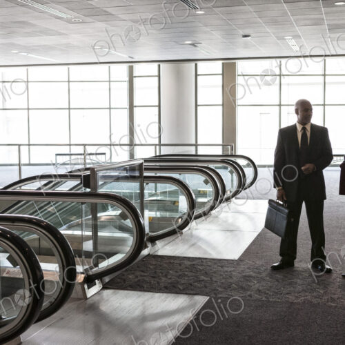 Two businesspeople, a man and woman standing talking by a bank of escalators in a…