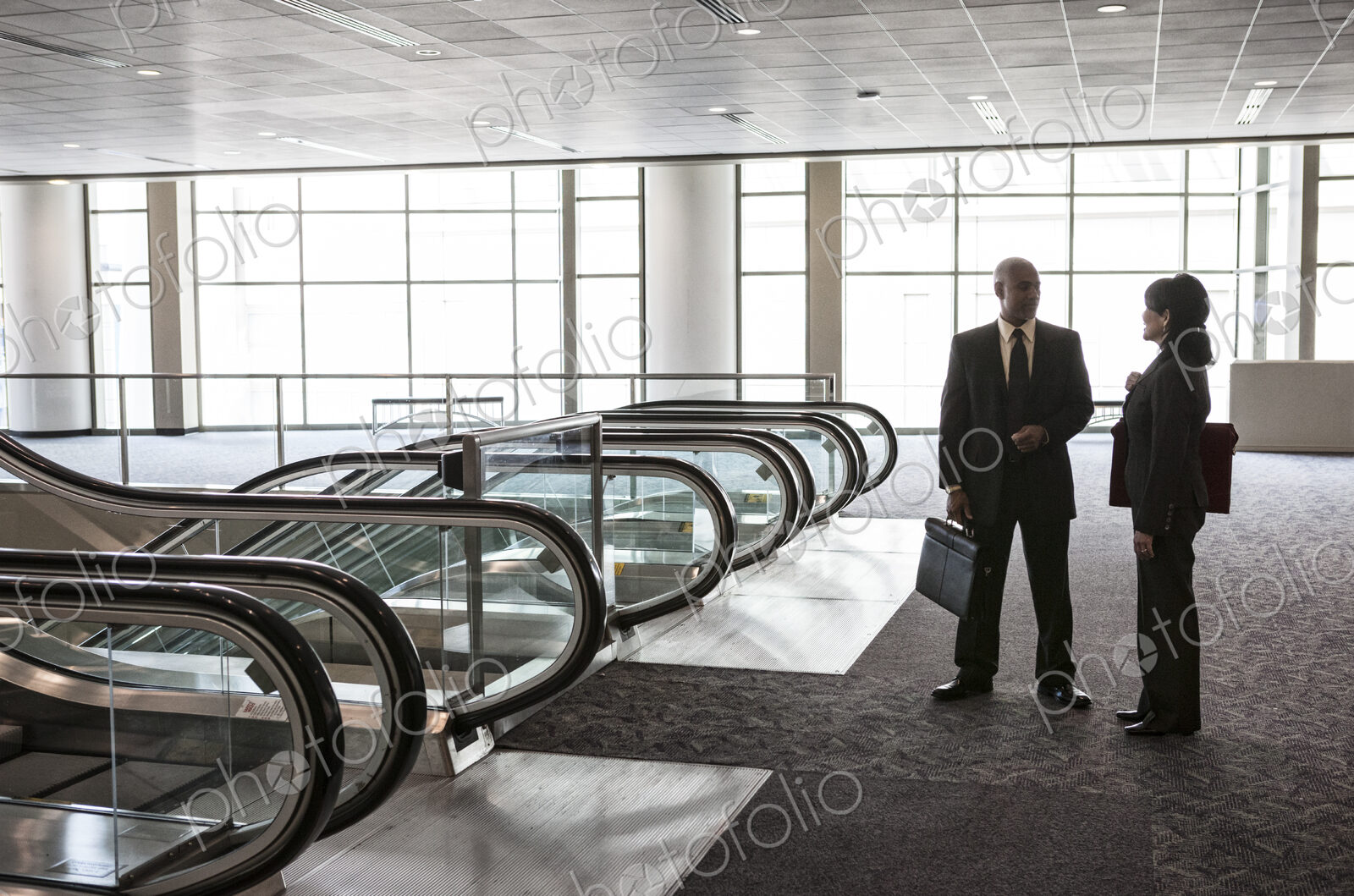 Two businesspeople, a man and woman standing talking by a bank of escalators in a…