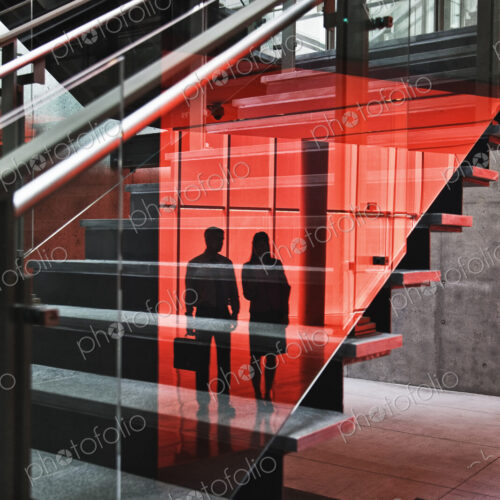 Two businesspeople shilouetted in reflections on the glass around a stairwell of a… Two businesspeople shilouetted in reflections on the glass around a stairwell of a…