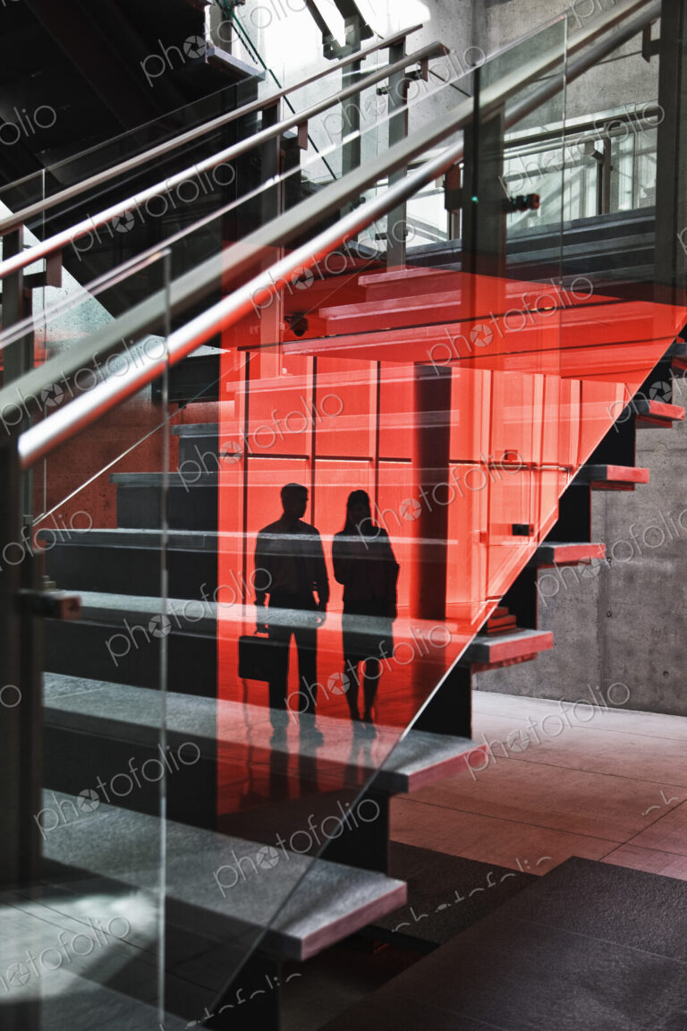 Two businesspeople shilouetted in reflections on the glass around a stairwell of a…