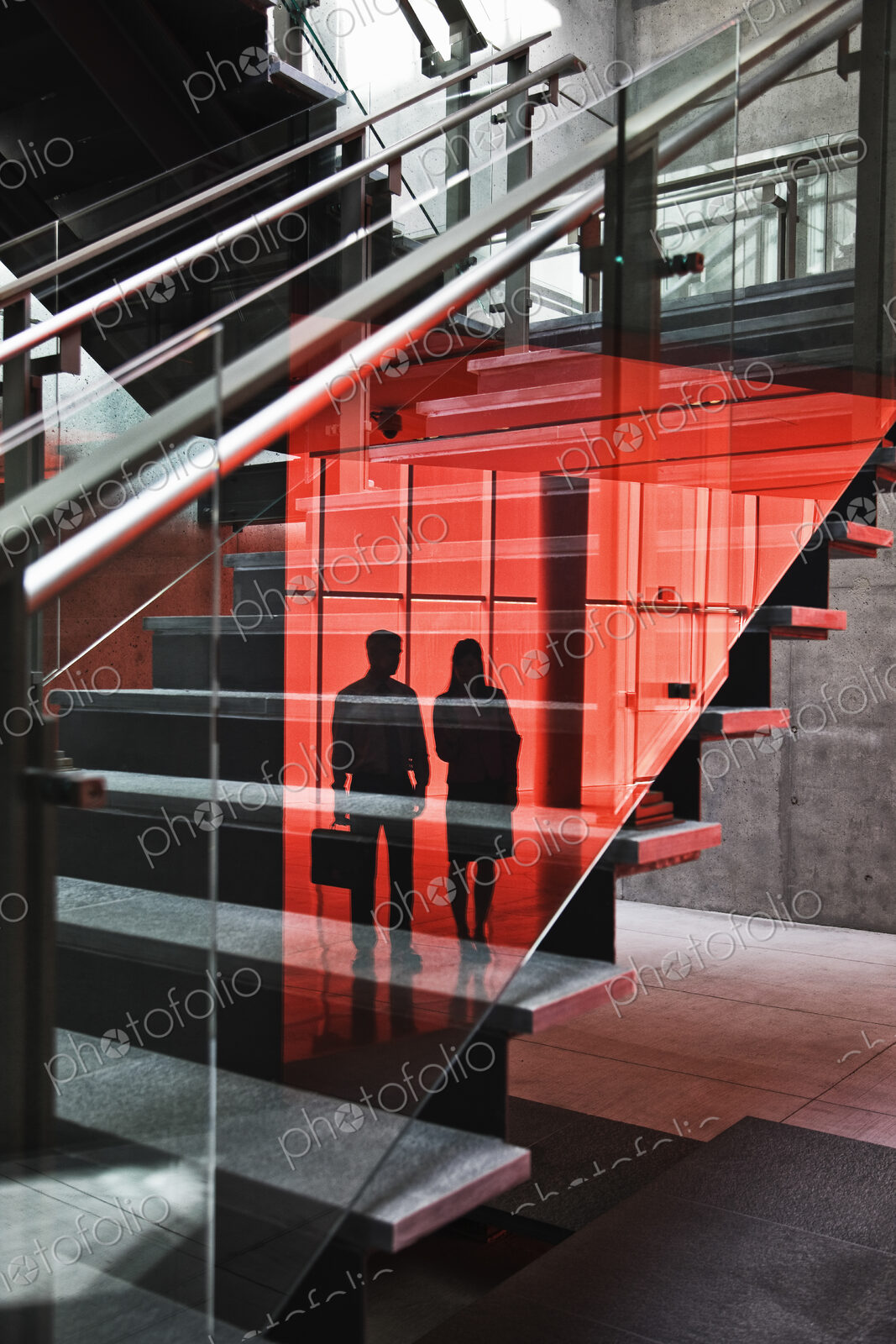 Two businesspeople shilouetted in reflections on the glass around a stairwell of a…