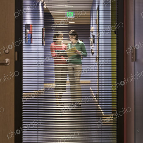 Two businesswomen walking down a hallway together. Two businesswomen walking down a hallway together.