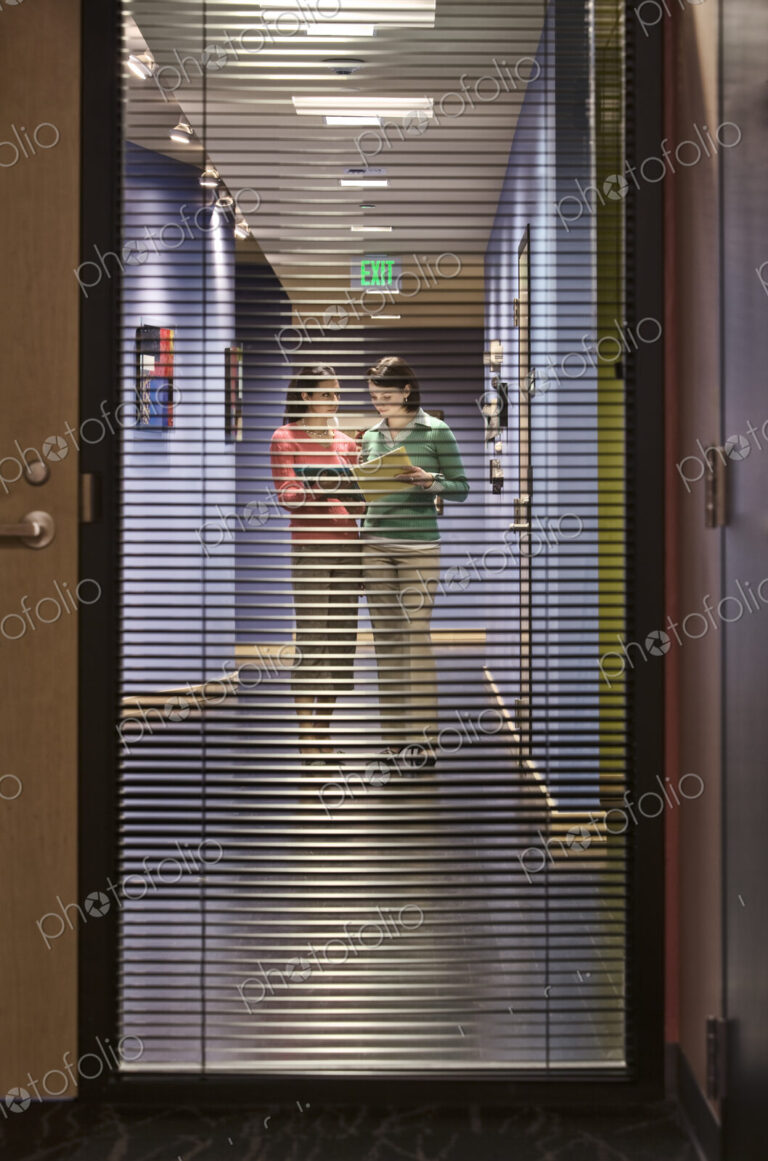 Two businesswomen walking down a hallway together.