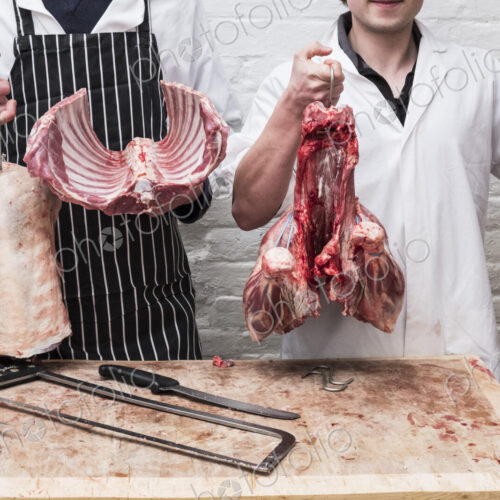 Two butchers at work holding up the butchered carcass of a spring lamb, ribs,… Two butchers at work holding up the butchered carcass of a spring lamb, ribs,…