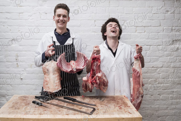 Two butchers at work holding up the butchered carcass of a spring lamp, ribs,…