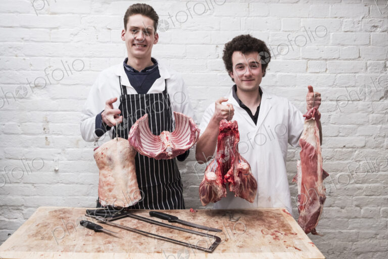 Two butchers at work holding up the butchered carcass of a spring lamp, ribs,…
