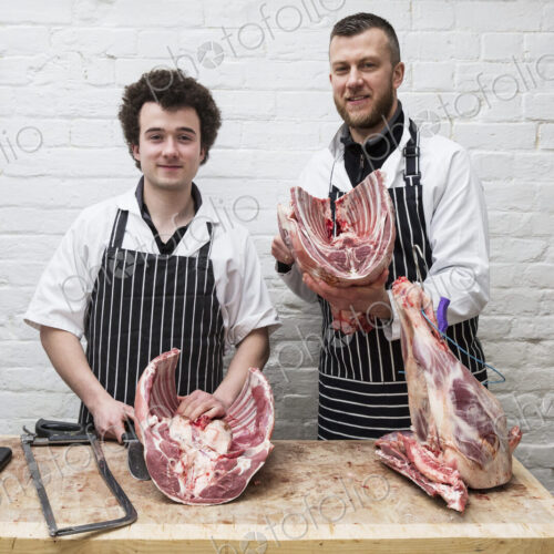 Two butchers side by side holding meat joints, part of a large butchered carcass. Two butchers side by side holding meat joints, part of a large butchered carcass.