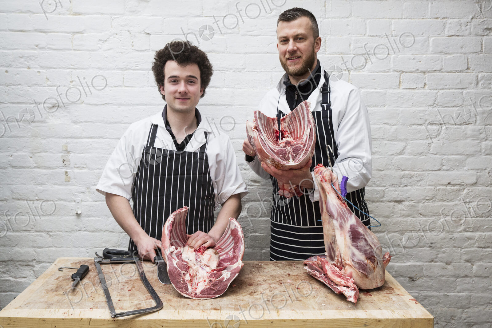 Two butchers side by side holding meat joints, part of a large butchered carcass.