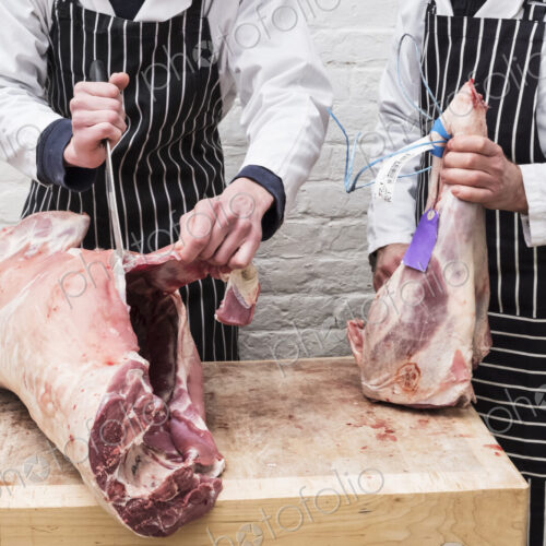 Two butchers working on butchering a lamb carcass for sale.