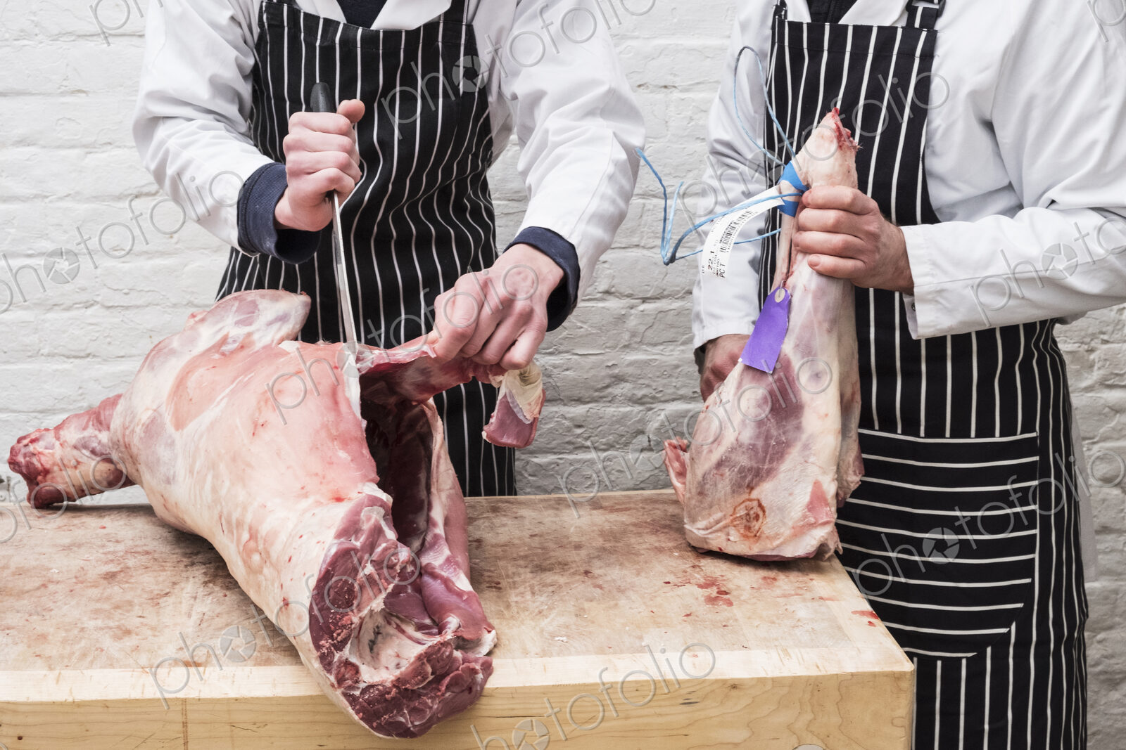 Two butchers working on butchering a lamb carcass for sale.