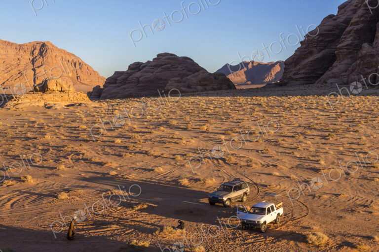 Two cars parked in desert landscape with rocks and mountains.