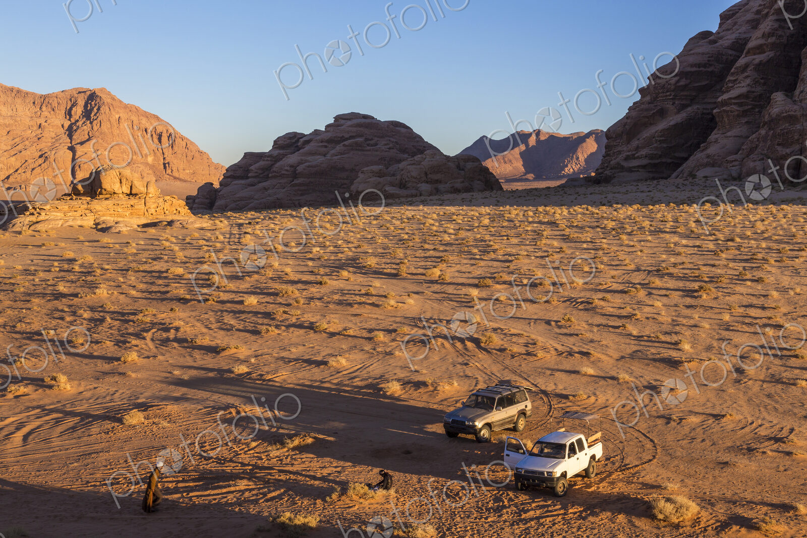 Two cars parked in desert landscape with rocks and mountains.