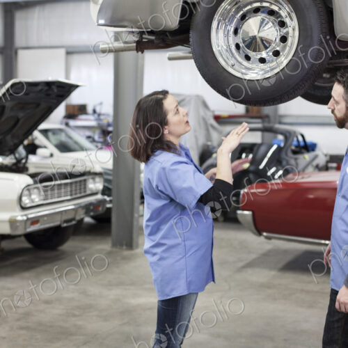 Two caucasian male and femal car mechanics at work on a car in a classic car repair shop.