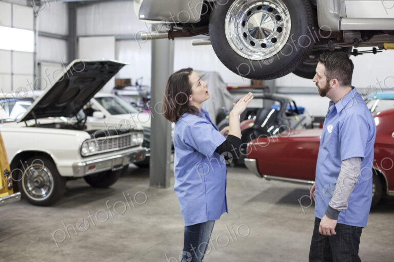 Two caucasian male and femal car mechanics at work on a car in a classic car repair shop.