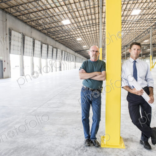 Two caucasian men standing in front of loading dock doors in a new warhouse interior. Two caucasian men standing in front of loading dock doors in a new warhouse interior.
