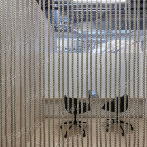 Two chairs in an office in a breakout area, view through a screen of vertical ropes. Two chairs in an office in a breakout area, view through a screen of vertical ropes.